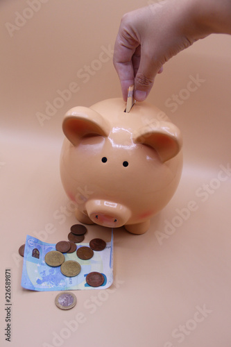 Hand introducing a coin into piggy bank with savings