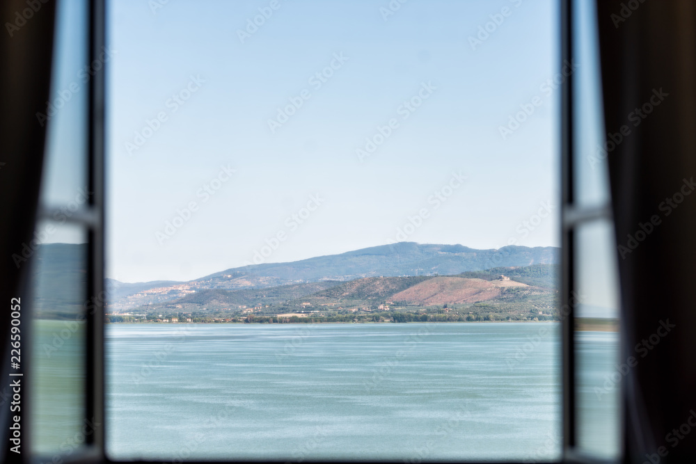 Lake Trasimeno in Castiglione del Lago, Umbria, Italy landscape view from open window in hotel during sunny summer day, blue turquoise water