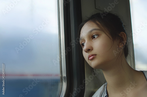 A sad young girl rides a train and looks out the window. © natavilman