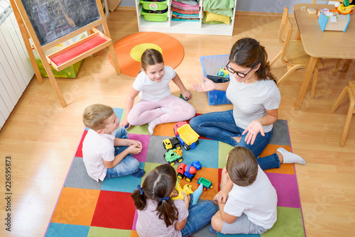 Preschool teacher talking to group of children sitting on a floor at kindergarten