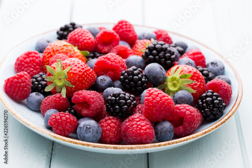 Fresh berry salad on blue dishes. Vintage wooden background.