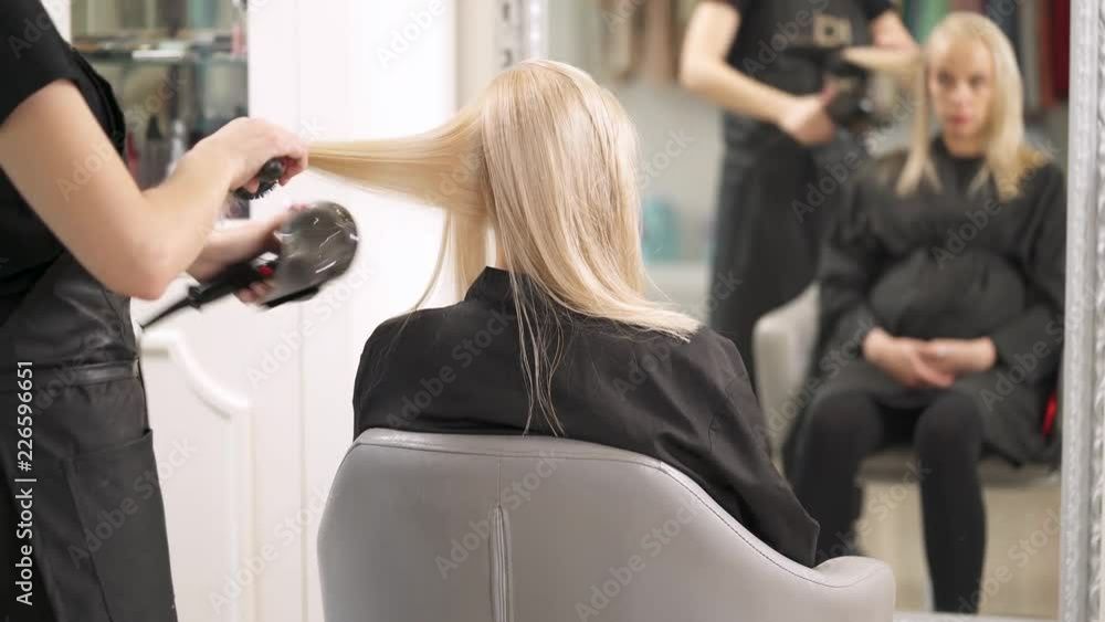 Pregnant blonde sits in the chair back to the camera. The hairdresser