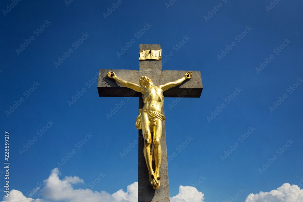 Golden Jesus Christ crucifixion statue, sunny summer day blue sky background, Vrbice, Moravia, Czech Republic