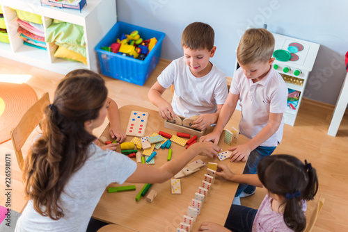 Obraz na plátně Preschool teacher with children playing with colorful wooden didactic toys at ki