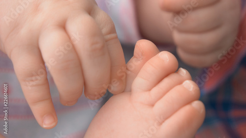 Close up hand and leg of infant baby. Hand of infant plays with feet close up. Baby care concept.