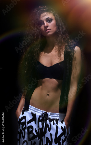 Beautiful young woman in hip-hop style against black wall photo