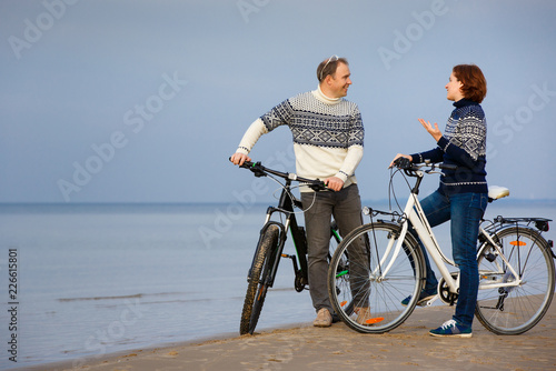 Cheerful young couple biking on beach outdoors