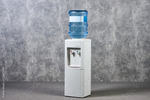 White water cooler gallon in office against gray textured wall background. International Exhibition furniture elements in large warehouse interior.