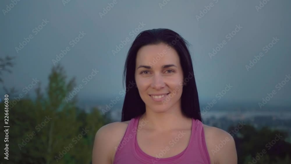 Portrait of an attractive sportswoman on the background of the city. Cute young woman with a sporty build is looking at the camera. Long-haired brunette posing against the backdrop of the sunset away Portrait of an attractive sportswoman on the background of the city. Cute young woman with a sporty build is looking at the camera. Long-haired brunette posing against the backdrop of the sunset away