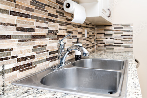 Modern clean kitchen room granite countertop, sink, faucet, cabinets in model house, home or apartment with paper towels decorative backsplash
