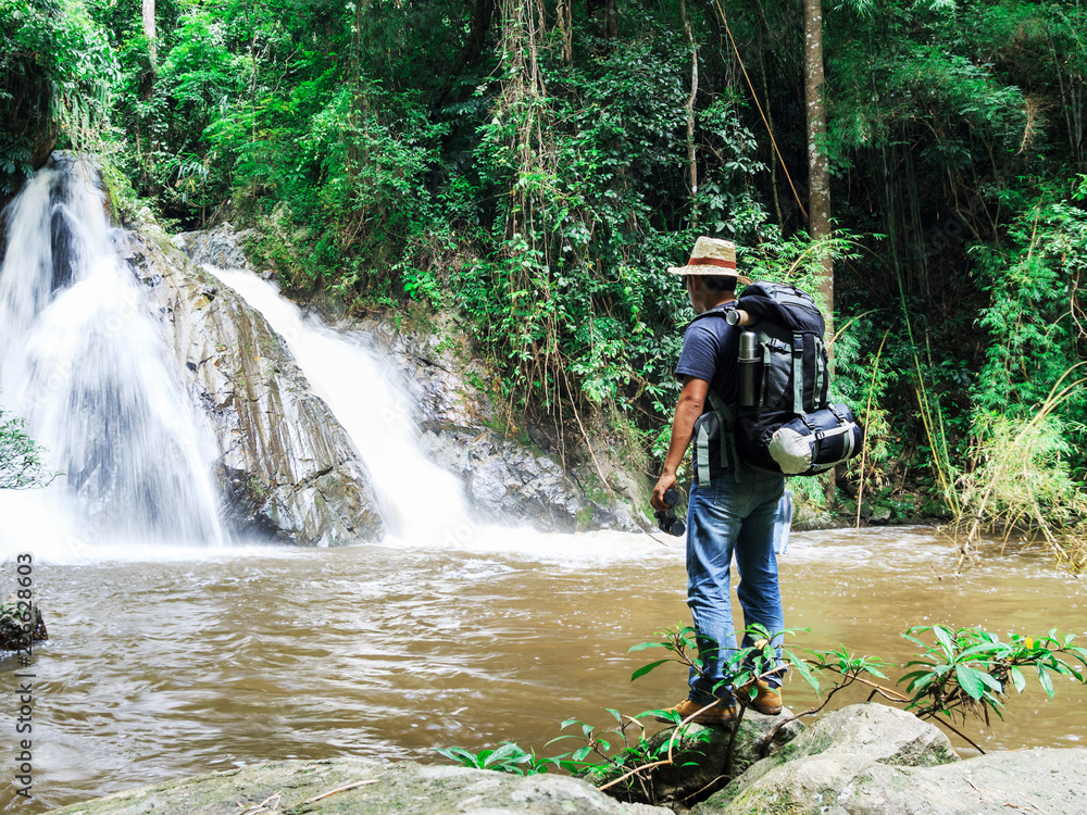 male hiker with backpack holding map looking nature waterfall in forest