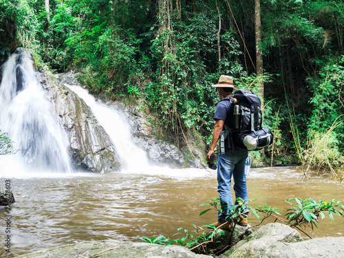 male hiker with backpack holding map looking nature waterfall in forest