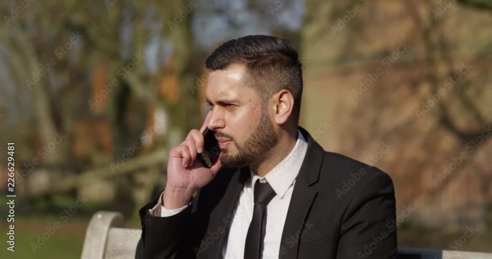 4K Attractive Asian businessman talking on phone outdoors in the park. Slow motion. 4K Attractive Asian businessman talking on phone outdoors in the park. Slow motion.