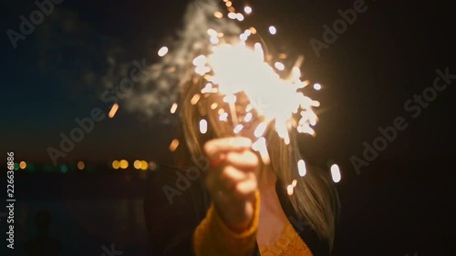 Overhappy Woman holding burning sparkler. Cheerful young woman holding two sparklers in hand outdoor celebrating new year's eve with set of bengal light