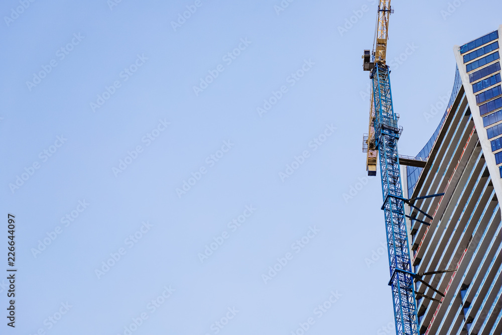 A high-rise building under construction and construction crane against blue sky. space for text