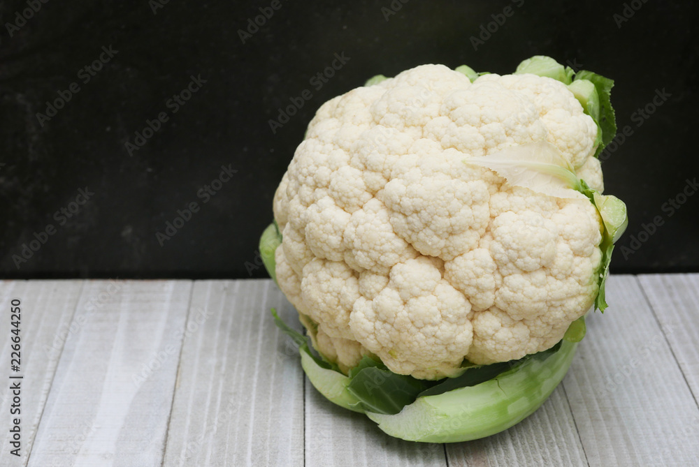 A head of cauliflower on a white wooden table against a black wall A head of cauliflower on a white wooden table against a black wall