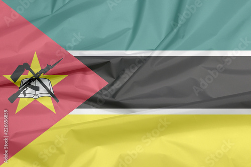 Fabric flag of Mozambique. Crease of Mozambican flag background  horizontal green black yellow and small white with red triangle bearing the yellow star an AK-47 assault rifle and the bayonet on book.
