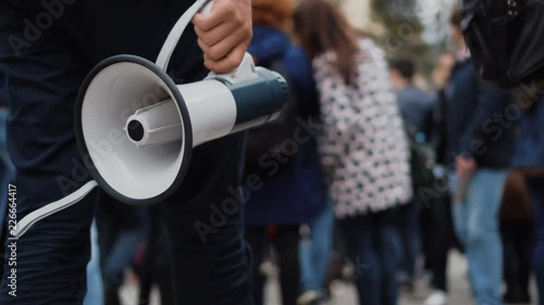 1 Man holds a megaphone in his hands, walking down street through many people on strike. Close up of one guy with loudspeaker in crowd at a demonstration 4k. Young adult boy on revolution. photo