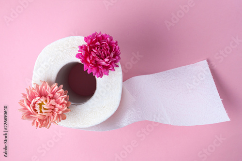 Scented toilet paper roll and a pink flowers on a pink background. Toilet paper with a smell. Hygiene
