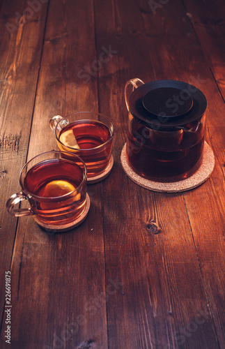 Two full cups and teapot of black tea with lemon, on brown wooden background top view, isolated, vertical