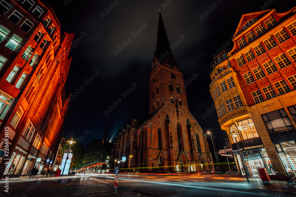 Night photography of Hamburg on the crossroad. View of St. Petri church and traditional red brick buildings. Long exposure. Car light trails. Hamburg, Germany
