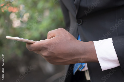 african business man hand using smartphone; hand of black businessman working with this smartphone, concept of mobile device technology, internet telecommunication; young adult african man hand model