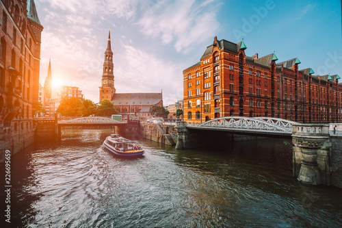Touristic cruise boat on a channel with bridges in the old warehouse district Speicherstadt in Hamburg in golden hour sunset light, Germany photo