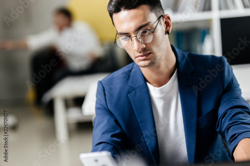 Professional young architect in glasses dressed in blue checkered jacket works on the laptop in the office
