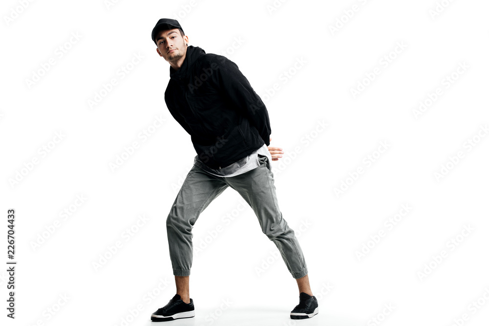 Young man wearing a black sweatshirt, gray pants, cap and sneakers dancing street dances on a white background Young man wearing a black sweatshirt, gray pants, cap and sneakers dancing street dances on a white background