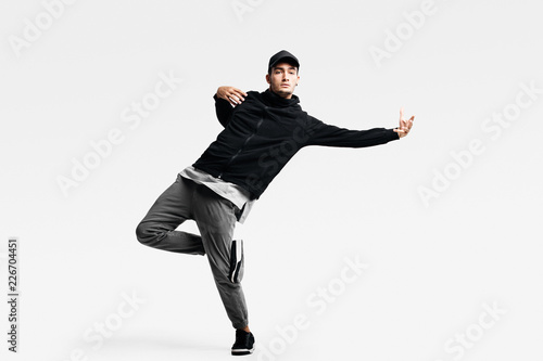 Handsome young man wearing a black sweatshirt, gray pants and a cap dancing street dances on a white background