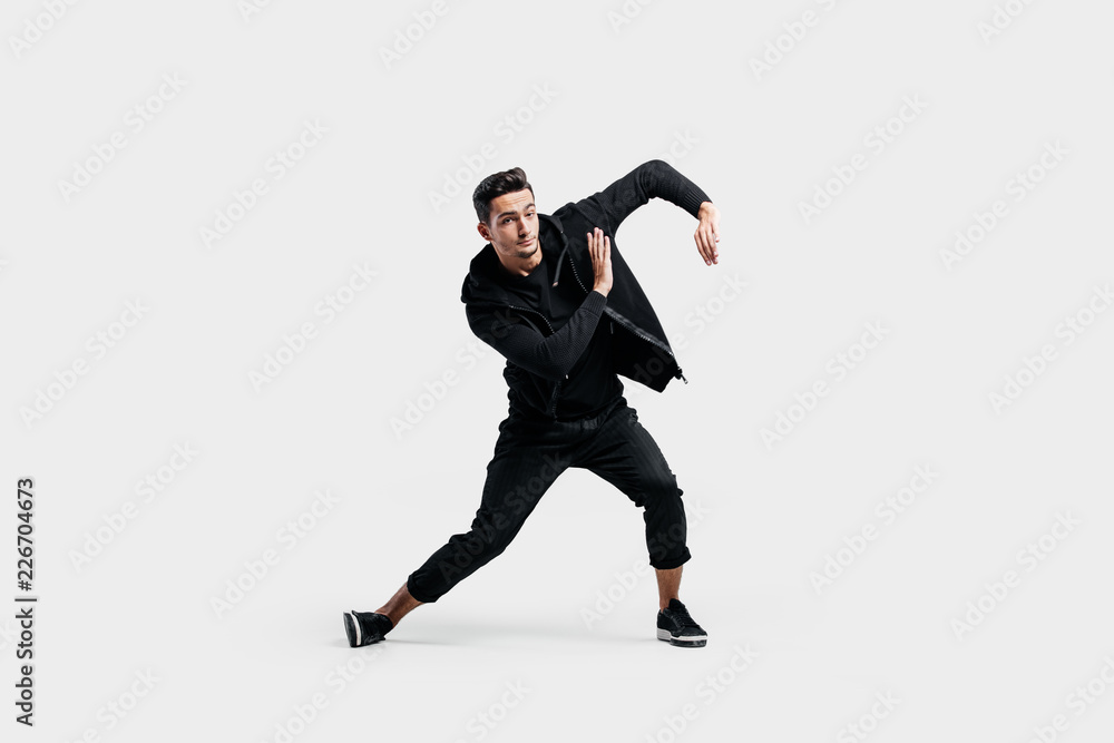 Handsome young  man dressed in a black clothes is dancing street dance. He makes stylized movements with his hands