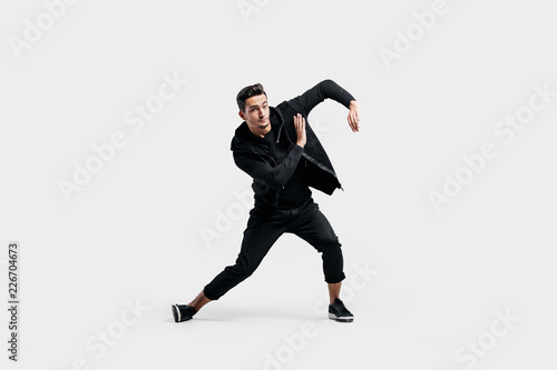 Handsome young man dressed in a black clothes is dancing street dance. He makes stylized movements with his hands
