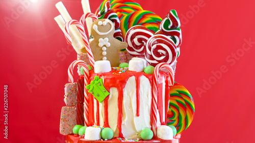 On trend festive candyland Christmas drip cake on red background.