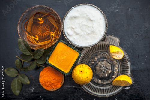 Close up of yogurt or curd face pack with honey,lemon juice,turmeric powder for acne skin on wooden surface in a glass container with raw lemon and turmeric powder.