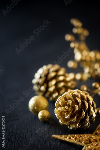 Gold pine cones on black wooden backgrouns with golden Christmas decoration. With copy space for your festive greeting
