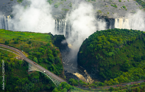 Victoria Falls in Zimbabwe and Zambia, Aerial helicopter photo, green forest around amazing majestic waterfalls of Africa. Livingston Bridge above the river