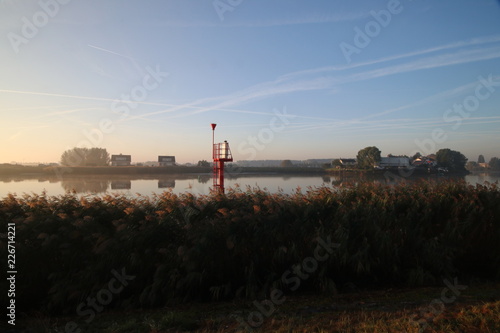Sunrise with colored aircraft trails  fog on the meadows and dyke at River Hollandsche IJssel in the Netherlands at nieuwerkerk.