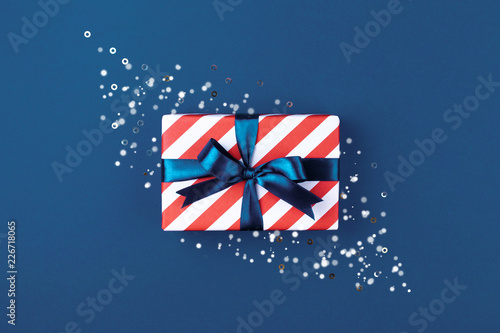 Gift box wrapped in red striped paper and tied with blue bow on blue backgrou...