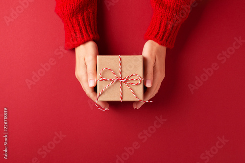 Female's hands in red pullover holding Christmas gift box on red background. Christmas and New Year concept.