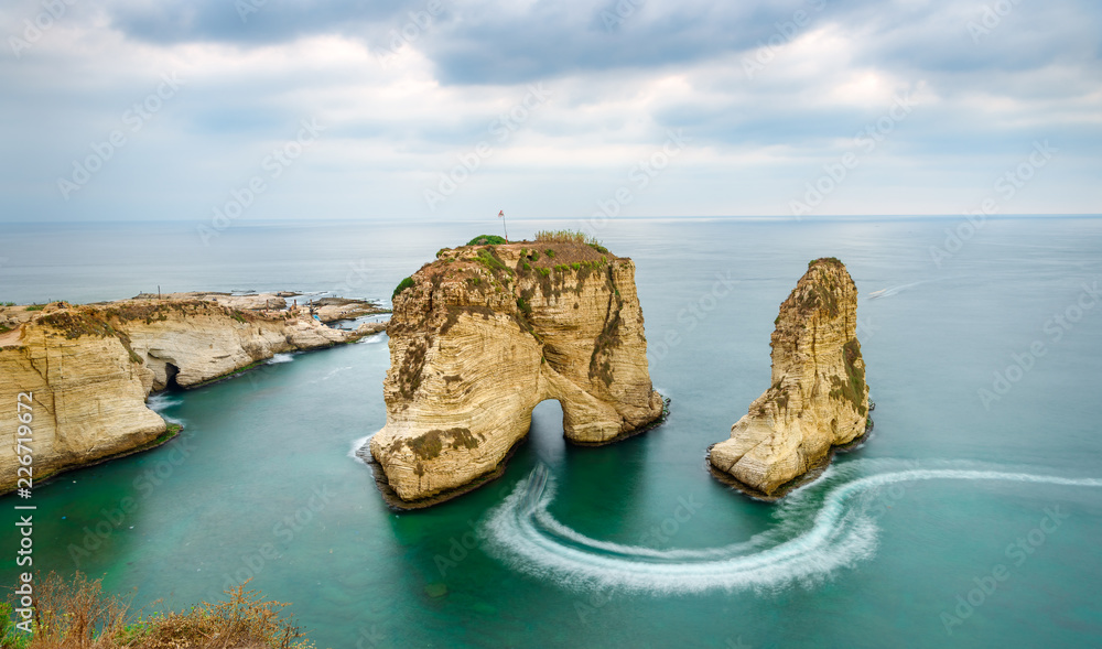 Naklejka premium Rouche skały w Bejrucie w Libanie w pobliżu morza i podczas zachodu słońca. Pochmurny dzień w Bejrucie w Libanie na Pigeon Rocks na Morzu Śródziemnym.