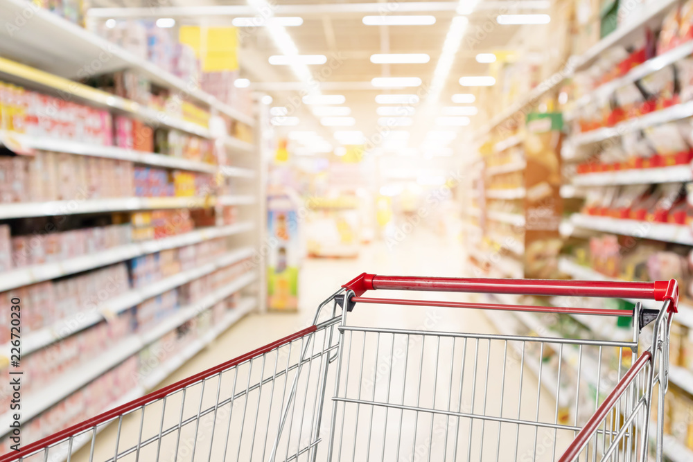 Empty shopping cart with abstract blur supermarket discount store aisle and product shelves interior defocused background - obrazy, fototapety, plakaty 