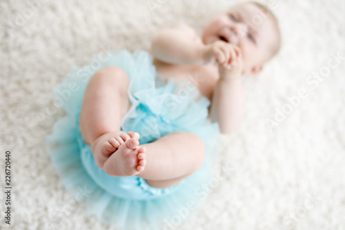 Close-up of legs and feet of baby girl on white background wearing turquoise tutu skirt.