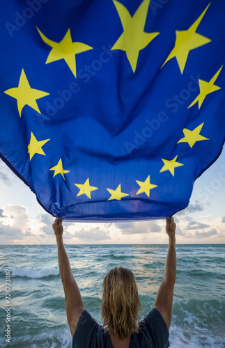 Man holding EU European Union flag in front of Mediterranean waves
