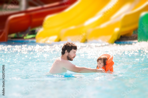 Happy family having fun together in outdoors swimming pool in water park (aquapark)