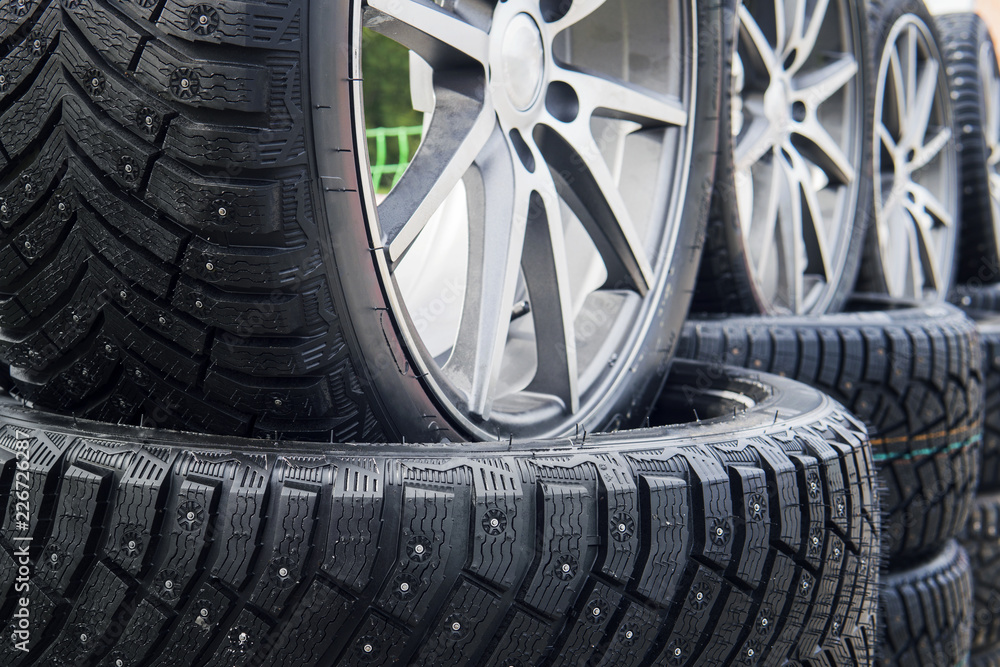 A close up of a lined winter studded wheels set outdoors. Close up of the studs and protectors on tires installed on the street. Winter tires positioned outdoors. Rows of exposed snow tires