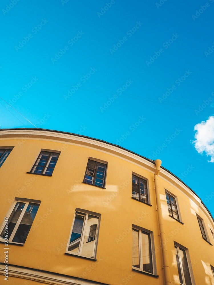 Parts of yellow round houses photographed from below against the blue clear sky in St. Petersburg
