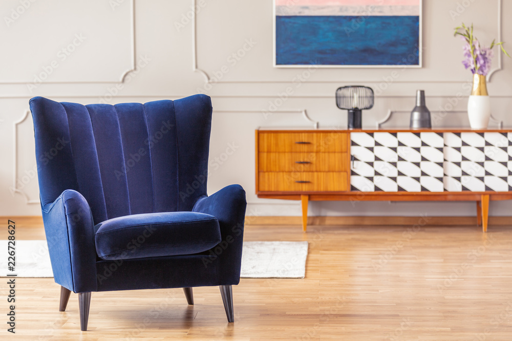 Fototapeta Zbliżenie na ciemnoniebieski fotel z zabytkową szafką w tle we wnętrzu salonu