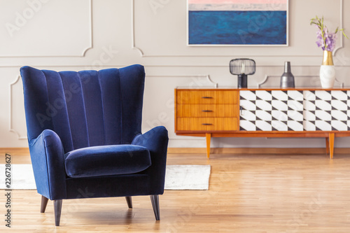 Close-up of a dark blue armchair with a vintage cabinet in the background in a living room interior