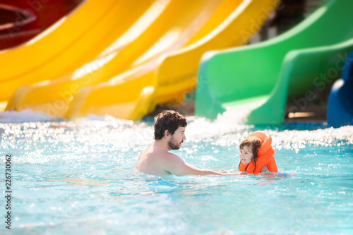 Happy family having fun together having fun on water slide in outdoors swimming pool in water park (aquapark)