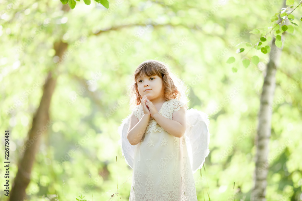 Beautiful little Angel girl standing at the forest with arms close to her chest as in prayer Beautiful little Angel girl standing at the forest with arms close to her chest as in prayer